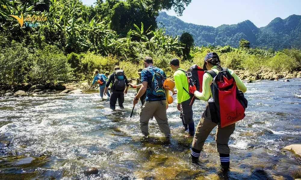 Travelers crossing a shallow river during a trekking adventure in Vietnam